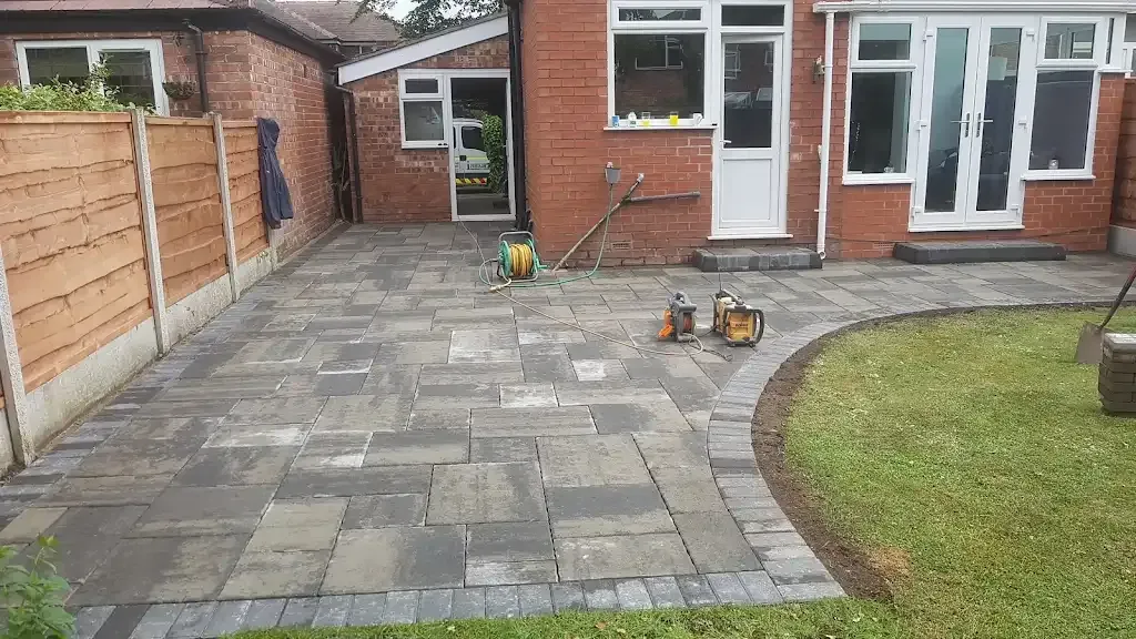 Newly laid grey and charcoal block paving patio or paved area next to a green lawn.