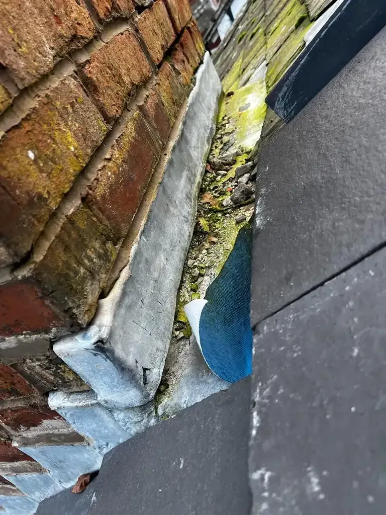Close-up of a roof valley with debris, lead flashing, and roof tiles, indicating a potential leak issue.
