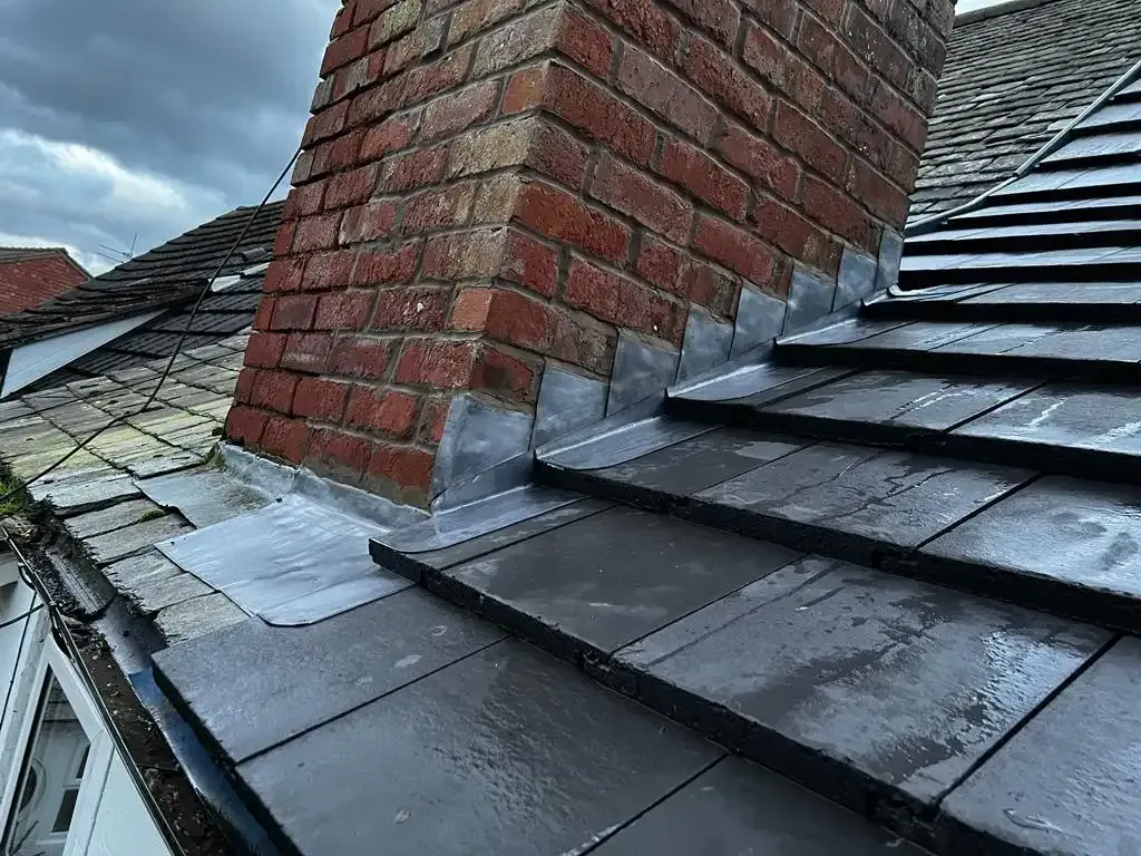 Newly installed lead flashing around a brick chimney on a dark tiled roof.