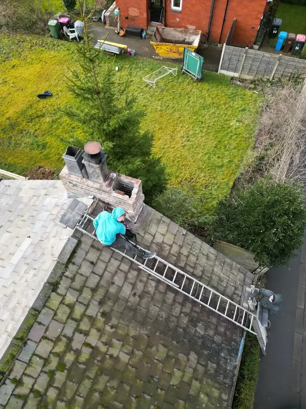 Two roofers on a tiled roof, one working near a chimney stack