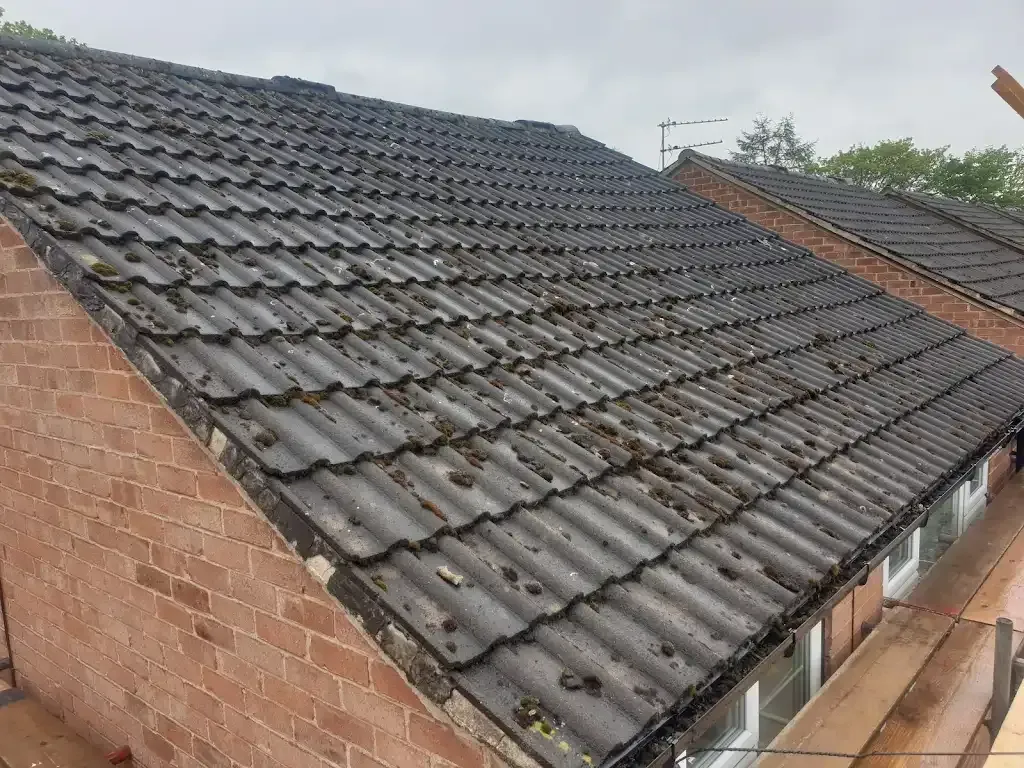 Tiled residential roof in Manchester with heavy moss and dirt, showing need for repair or cleaning.