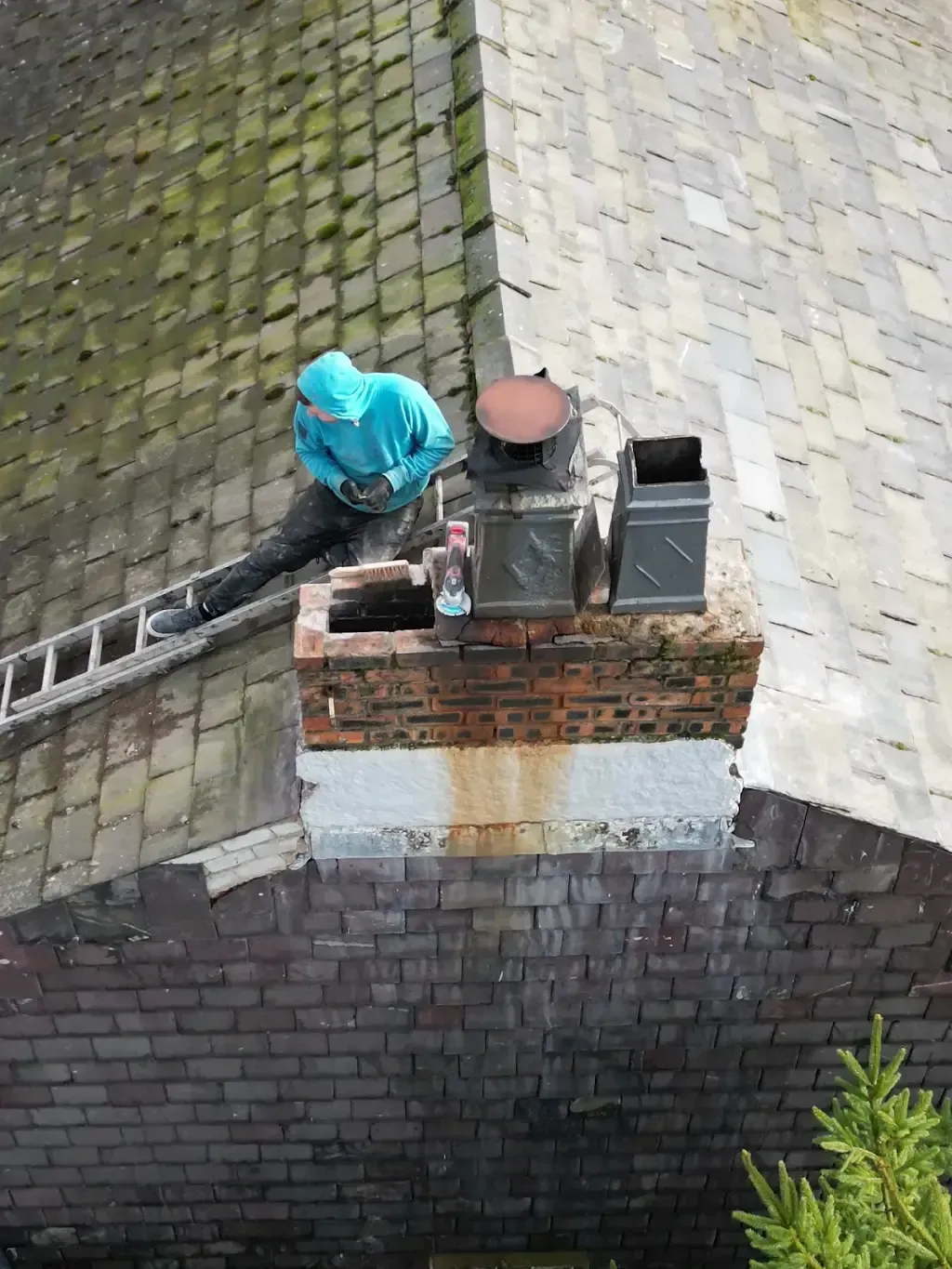 A roofer working on a chimney on a tiled roof with a ladder.