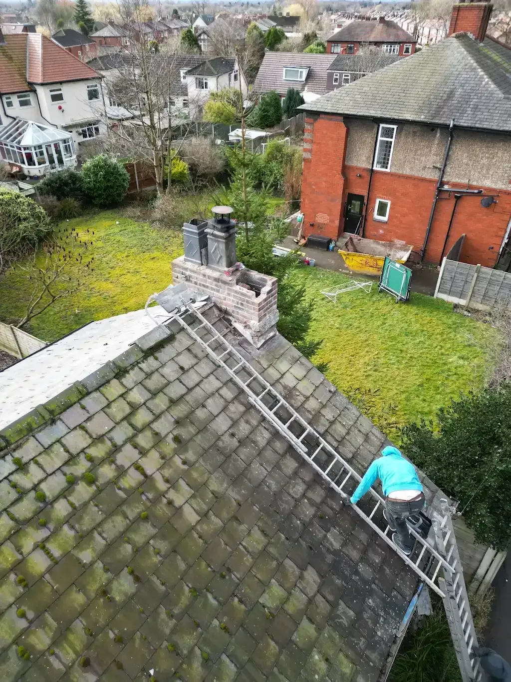 Roofer working on a tiled roof in Manchester, showing a ladder and chimney.