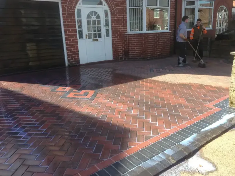 Newly installed block paving driveway with decorative borders and two contractors sweeping sand